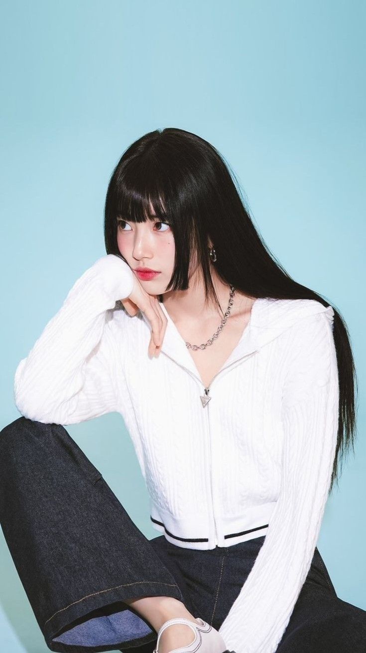 a woman sitting on the floor with her legs crossed and wearing white sweater and jeans