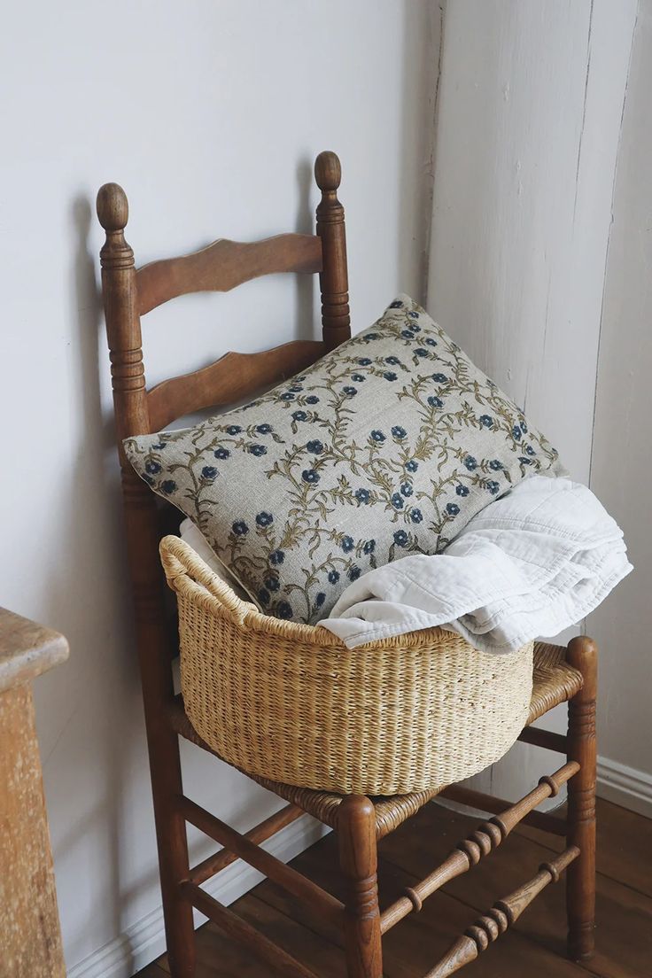 a basket sitting on top of a wooden chair next to a pillow and some pillows