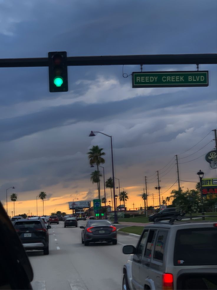 a green traffic light hanging over a street filled with lots of cars and palm trees