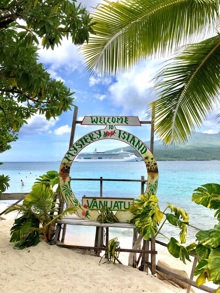 a sign that is on the side of a beach near some water and palm trees