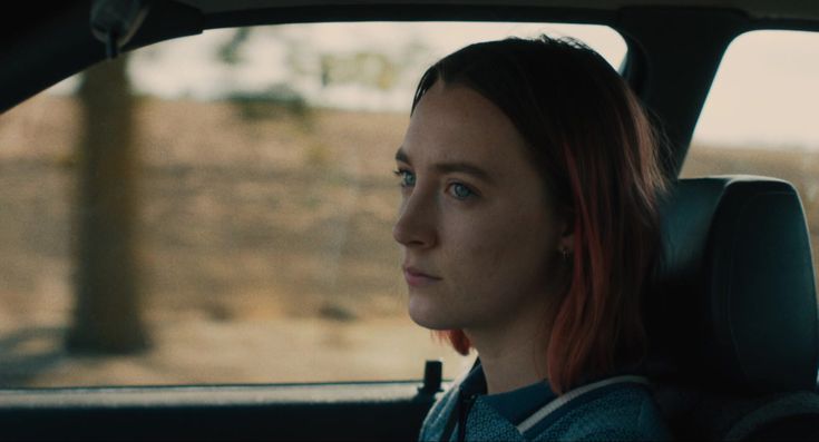 a woman with red hair sitting in the back seat of a car, looking off into the distance