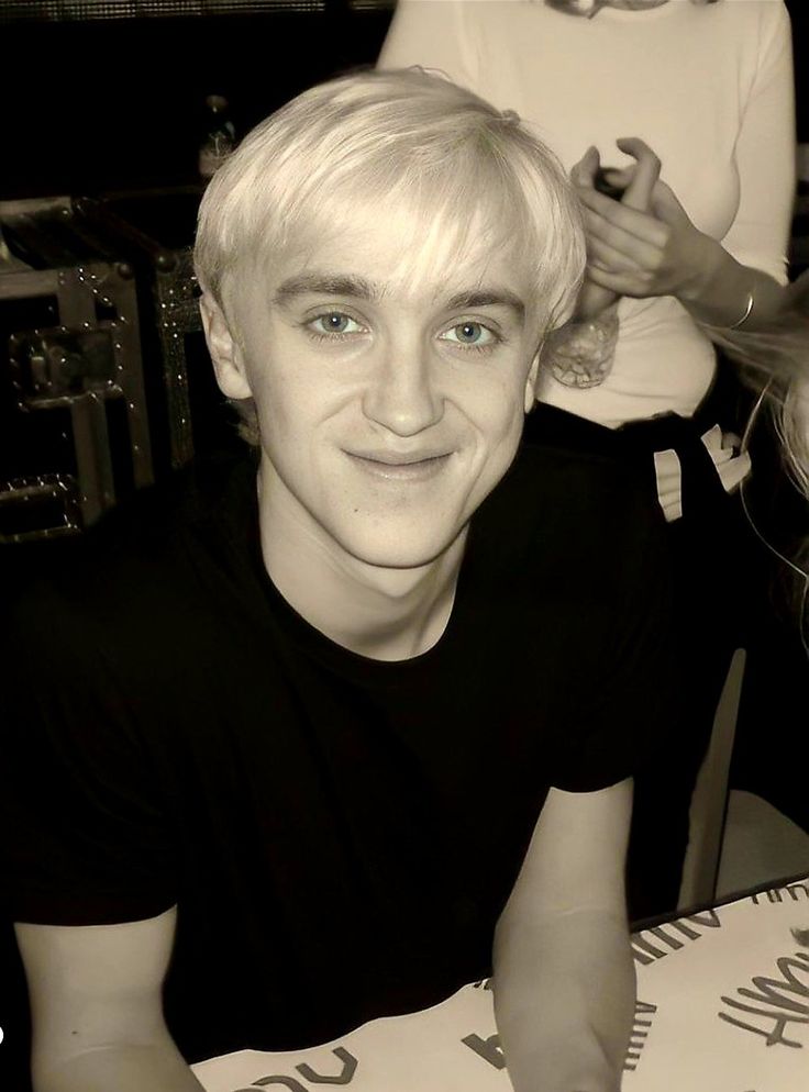 a young man with blonde hair sitting at a table in front of a pizza box