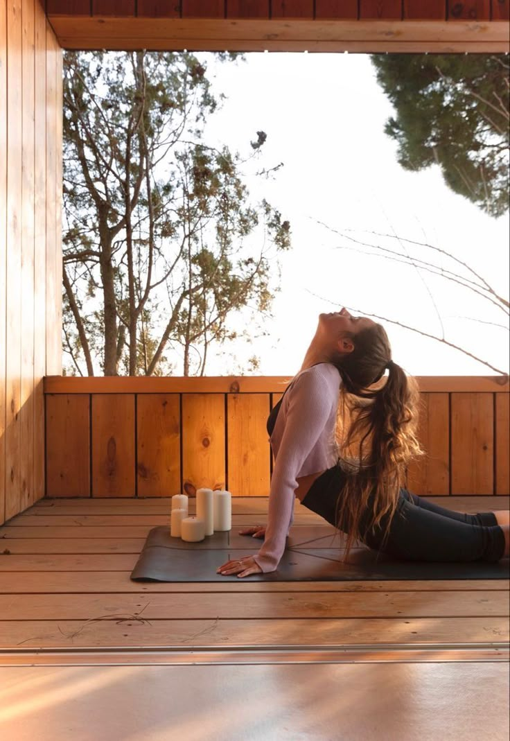 a woman is doing yoga on a mat in front of a wooden wall and trees