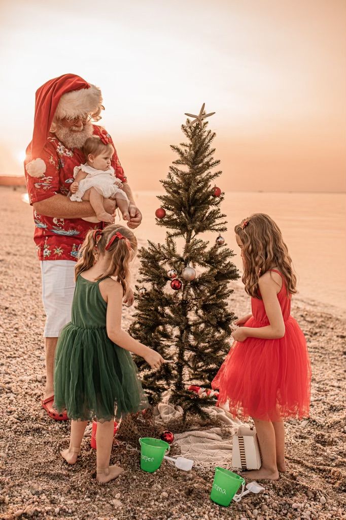 two girls and an old man decorate a christmas tree on the beach