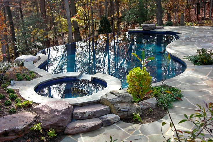 an outdoor swimming pool surrounded by rocks and trees in the fall season, with water flowing from it