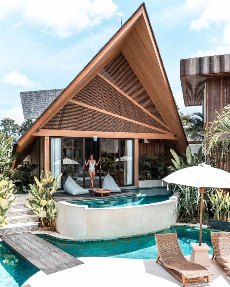 a woman is sitting on the edge of a swimming pool in front of a house