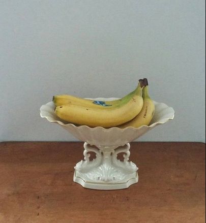 two bananas in a white bowl on a wooden table