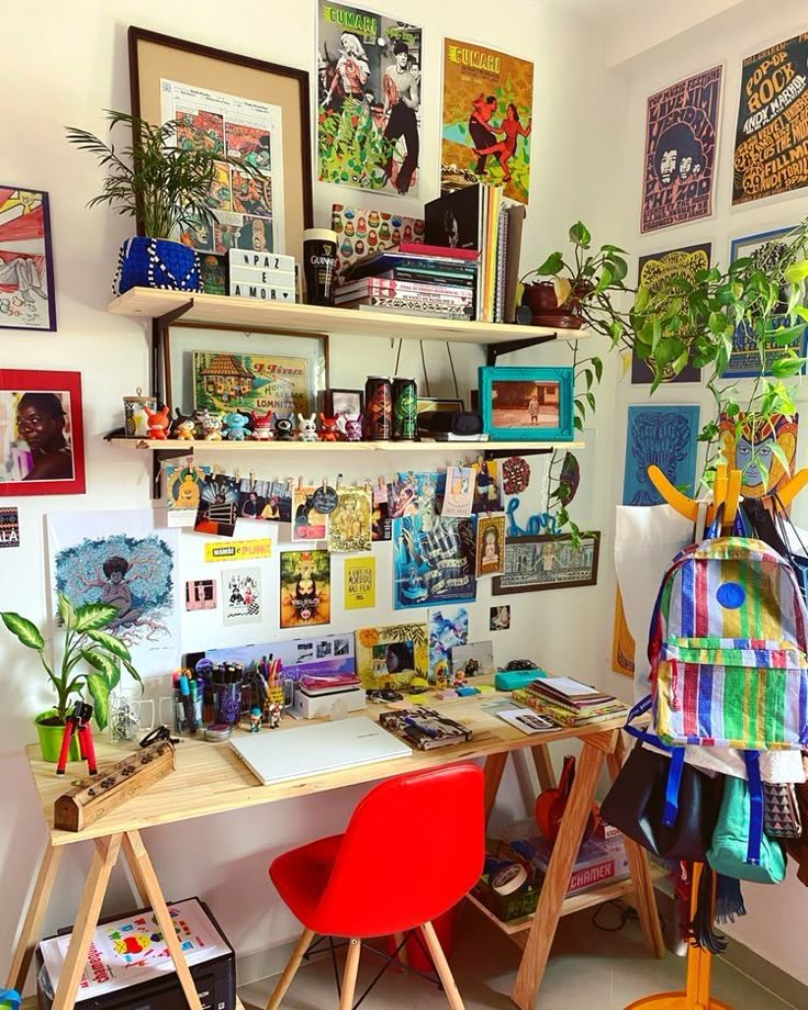 a desk with some books and pictures on the wall above it, next to a red chair