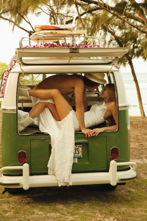 a man and woman laying on the back of a green vw van in front of palm trees