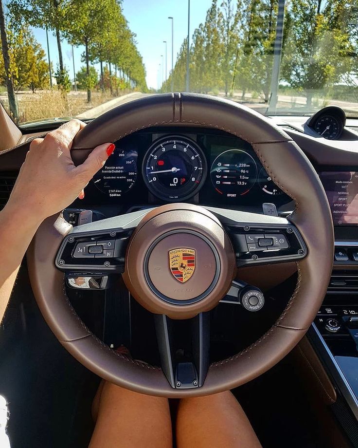 a woman is sitting in the driver's seat of a porsche car with her hands on the steering wheel