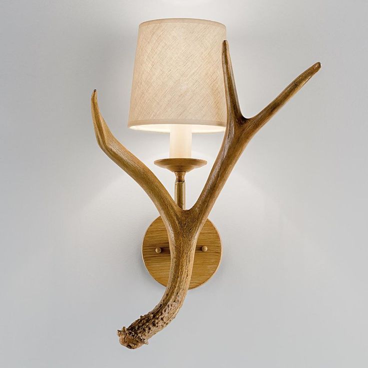 a deer antler wall light with a white shade on it's head and the bulb turned off