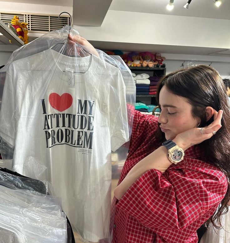 a woman is looking at a t - shirt in a clothing store while holding it up to her ear