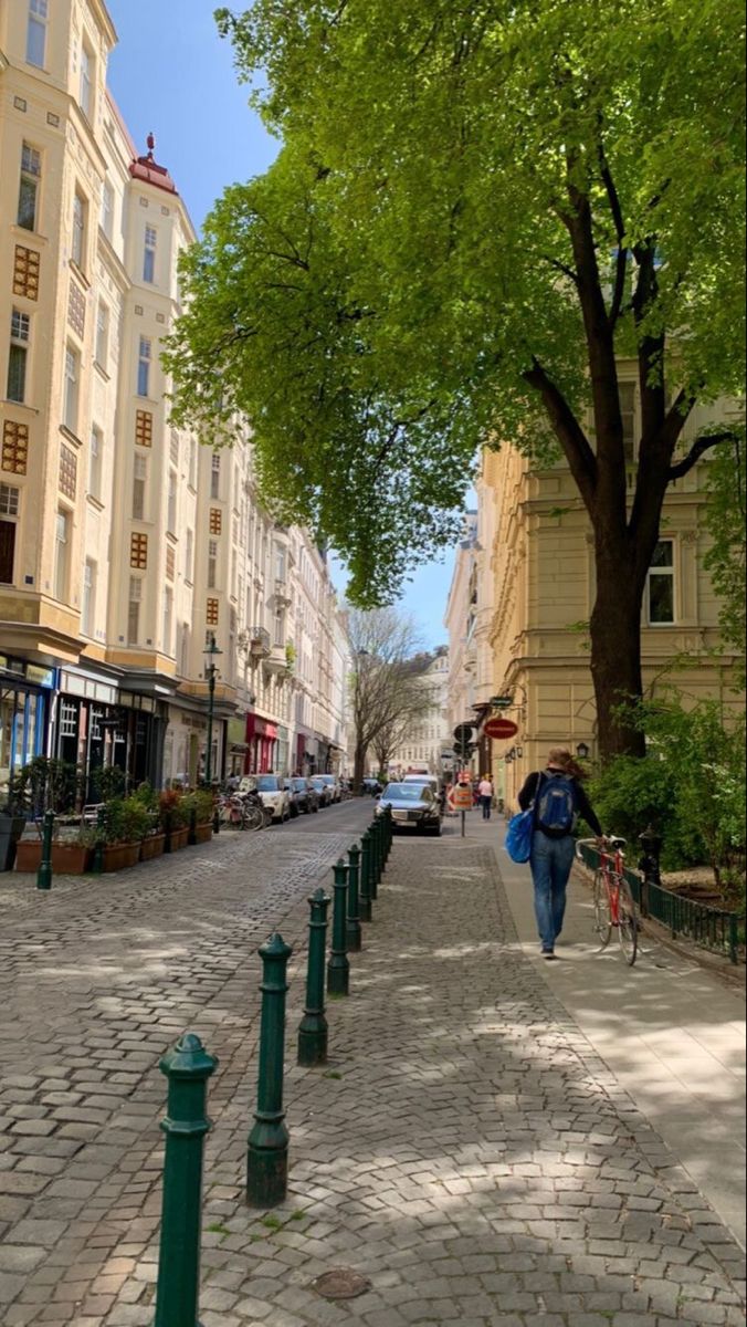 a woman walking down the street with an umbrella in her hand and trees lining the sidewalk