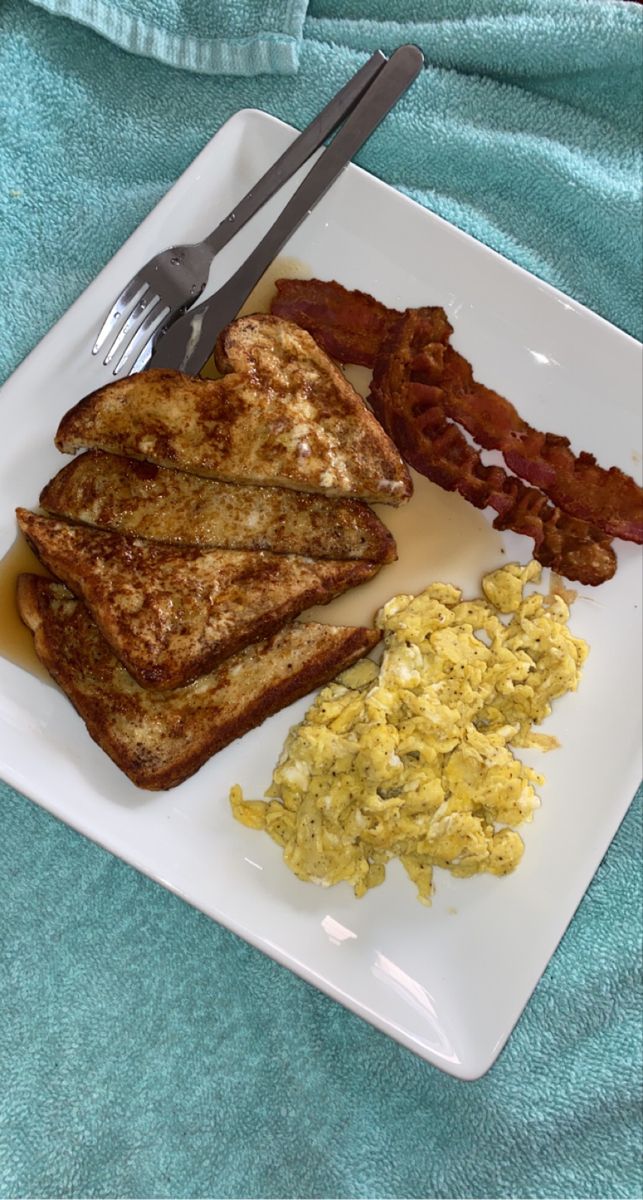 a white plate topped with toast, eggs and bacon next to a knife and fork