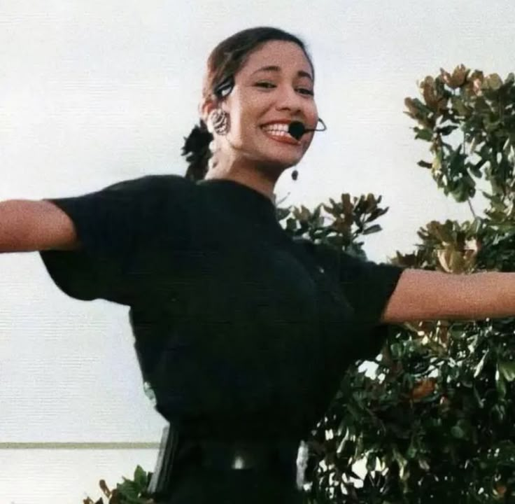 a woman is smiling and holding her arms out to the side while standing in front of a tree