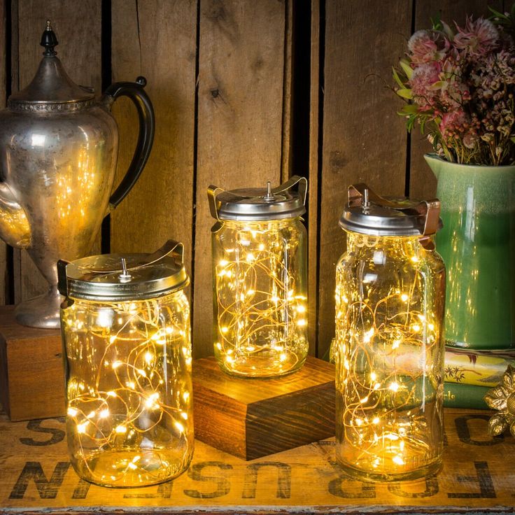 three mason jars with fairy lights in them sitting on a table next to a teapot