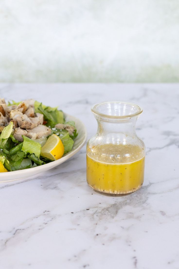 a bowl of salad next to a bottle of dressing on a marble counter top with a white plate