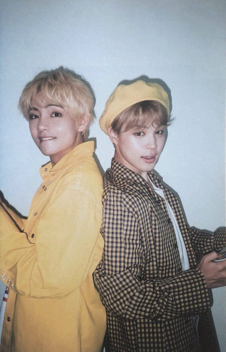 two young men standing next to each other in front of a white wall and wearing yellow hats