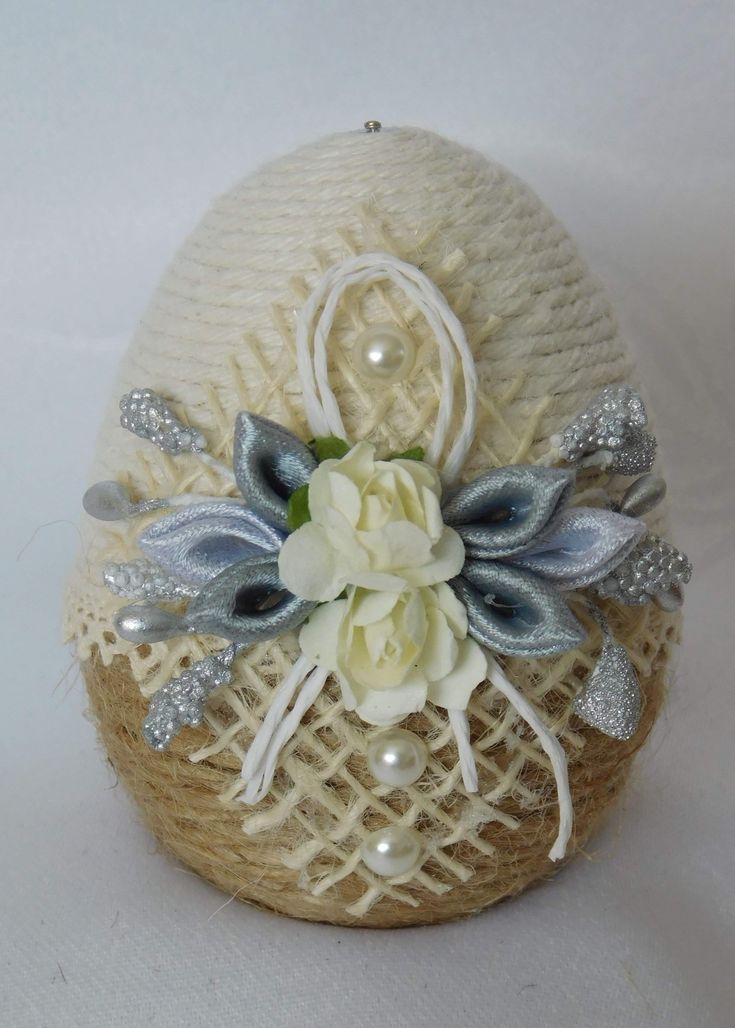 an egg decorated with flowers and pearls on a white tablecloth covered basket ornament