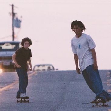 two young men riding skateboards down a street