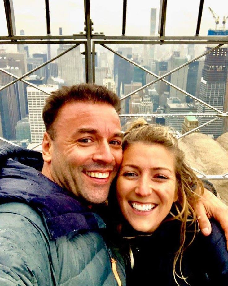 a man and woman taking a selfie on top of the empire building in new york city