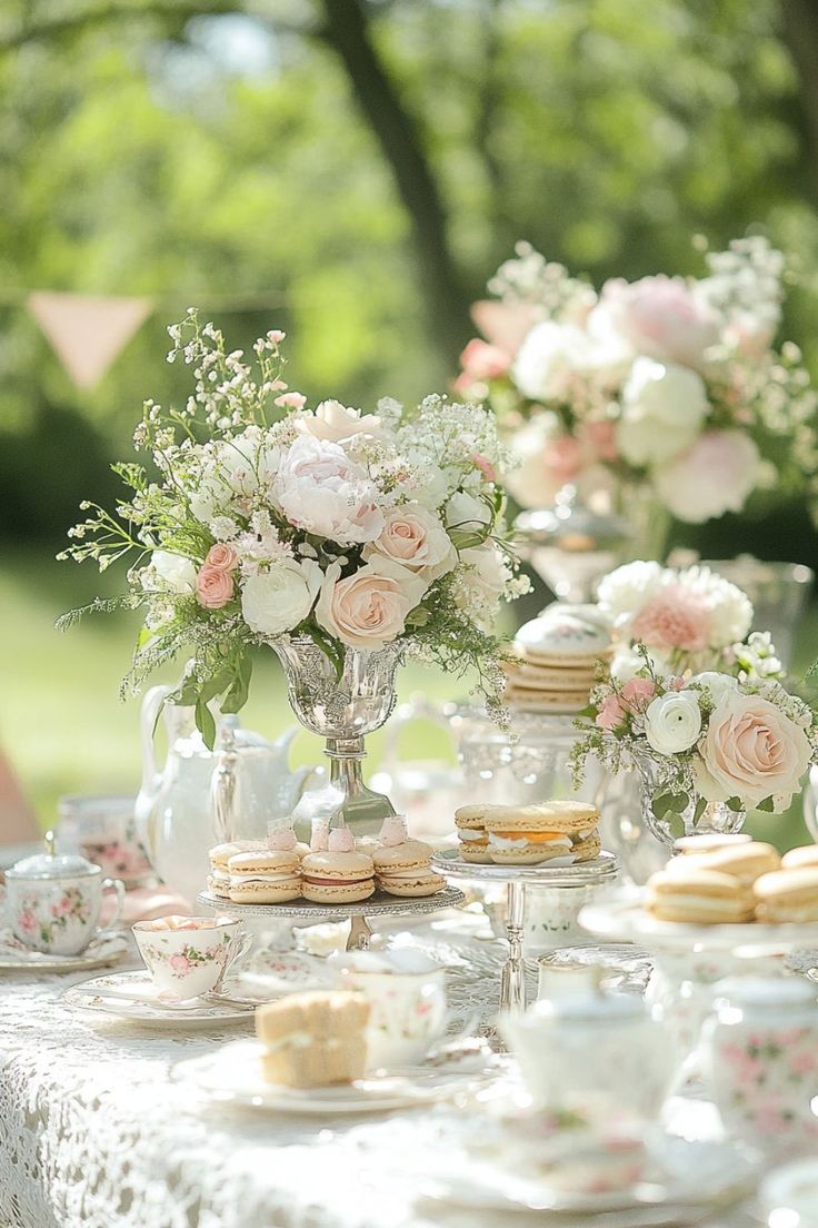 a table topped with lots of white and pink flowers next to teacups filled with cookies