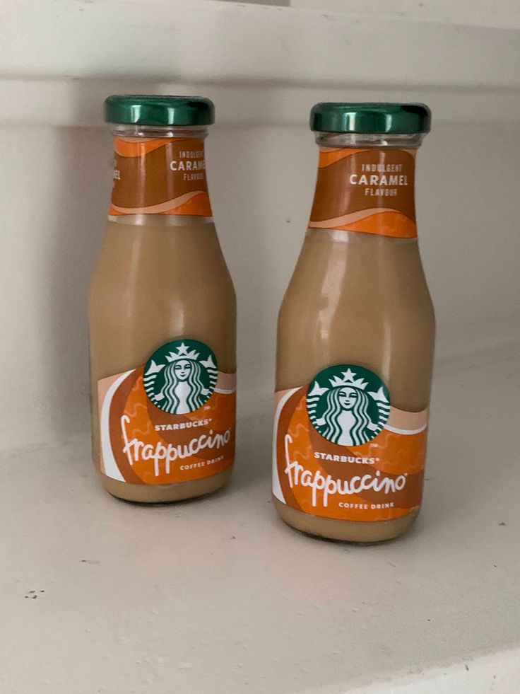 two bottles of starbucks coffee sitting on top of a white counter next to each other