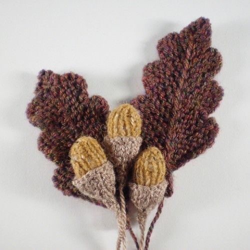 two knitted acorns with brown and yellow leaves attached to them on a white surface