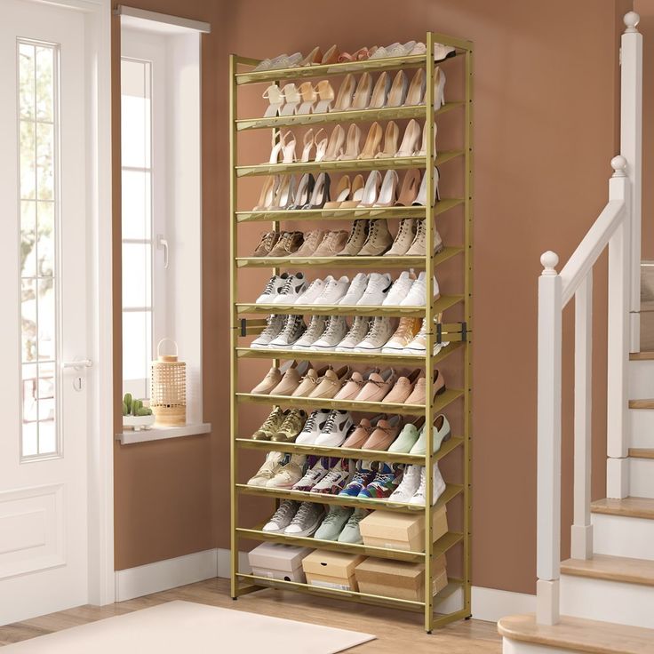 a gold shoe rack filled with pairs of shoes next to a stair case in a room