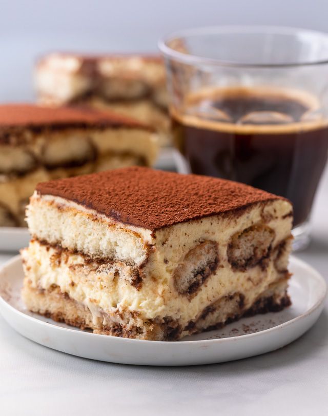 a piece of cake sitting on top of a white plate next to a cup of coffee