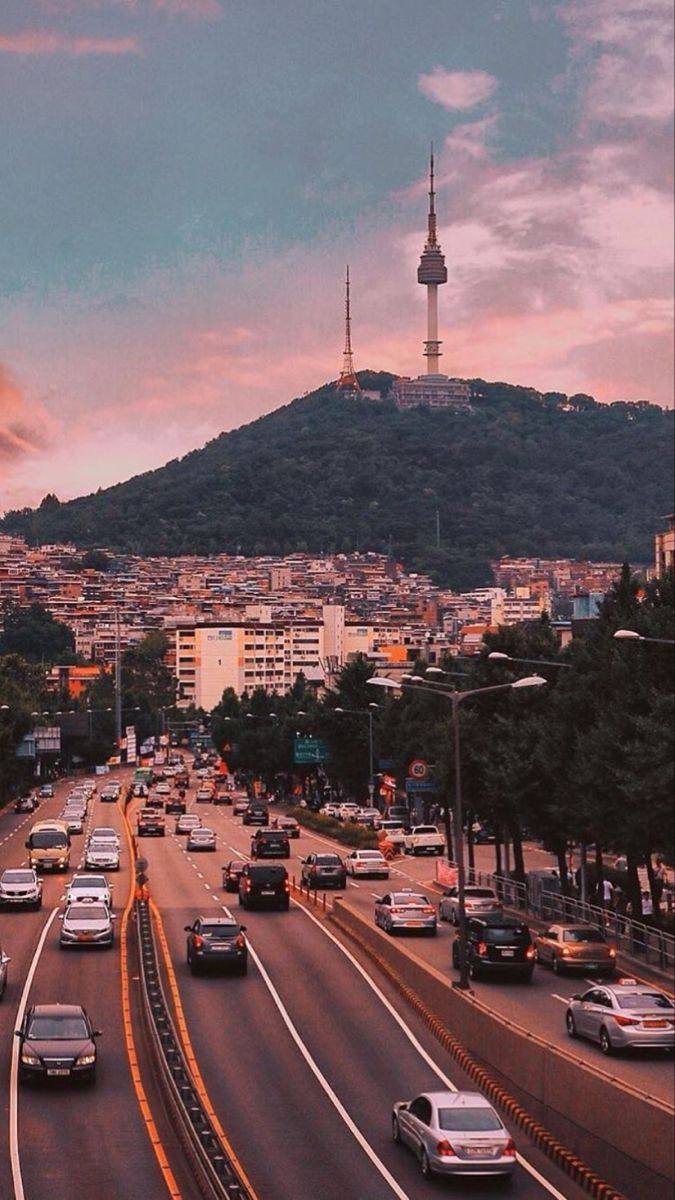 cars are driving down the road in front of a hill with a tower on top