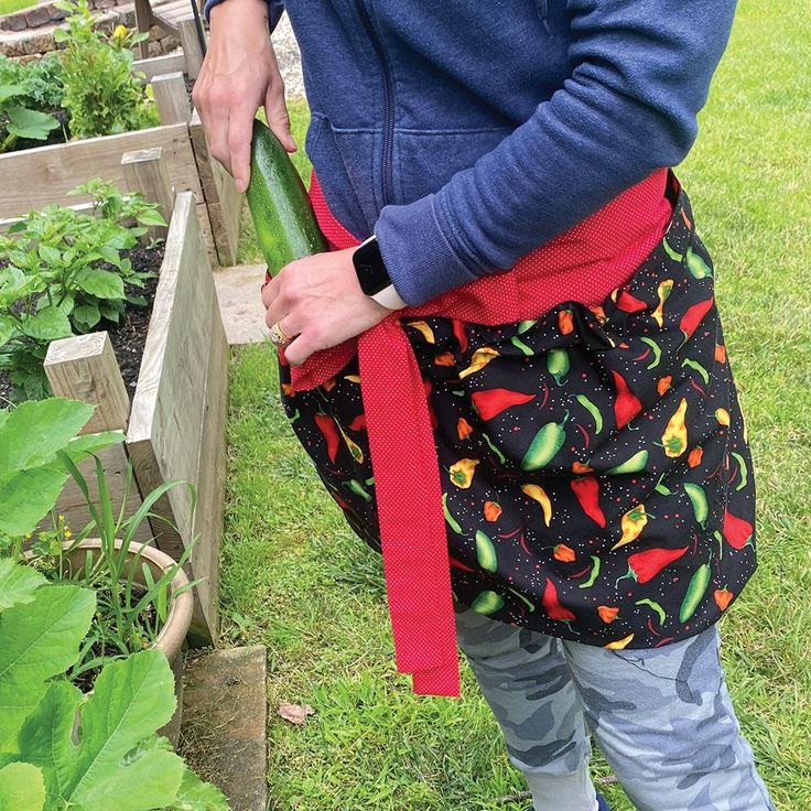 a woman holding a cucumber in her hand while standing next to a garden