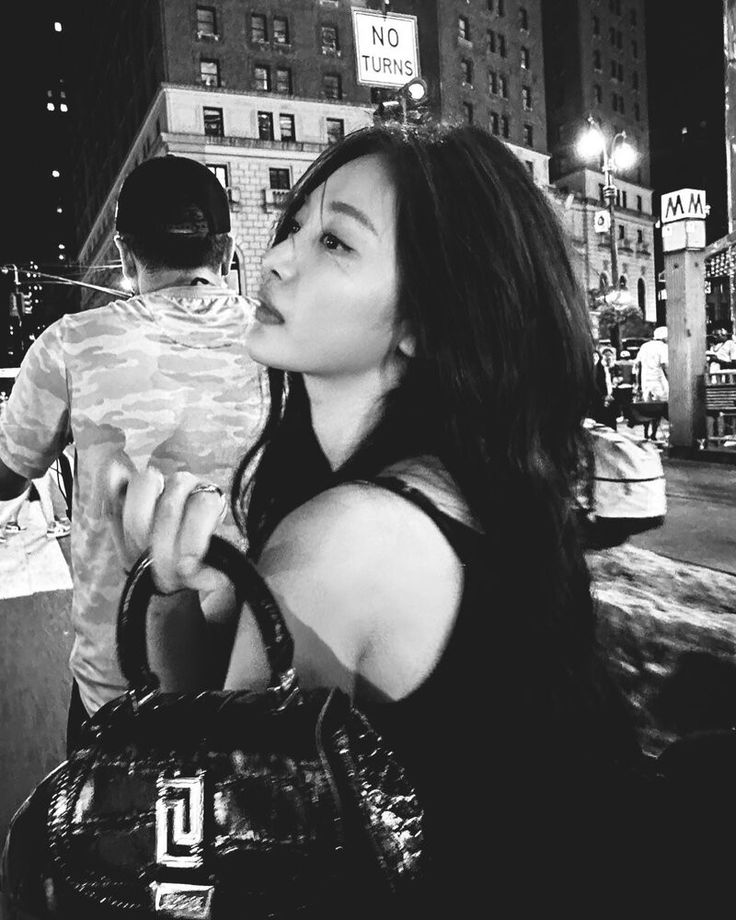 a black and white photo of a woman holding a handbag in the city at night