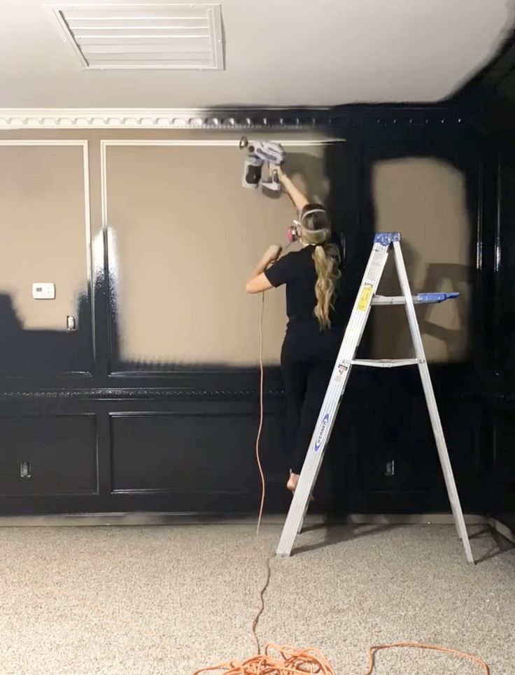 a woman standing on a ladder with a paint roller in front of her and painting the walls