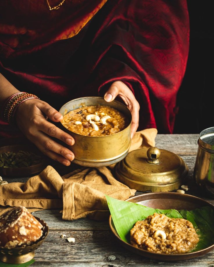 a woman holding a bowl of food on top of a wooden table next to other dishes