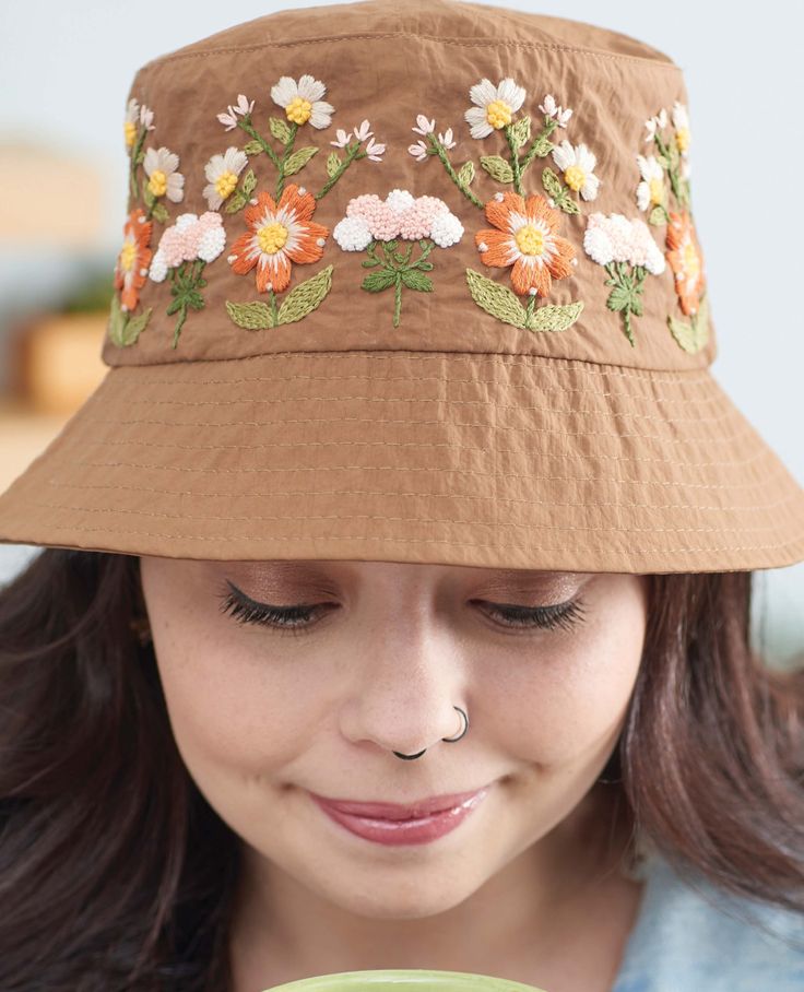 a woman wearing a brown hat and holding a green cup in her hand with flowers on it