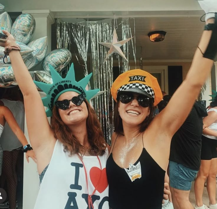 two women wearing hats and sunglasses pose for a photo in front of the statue of liberty