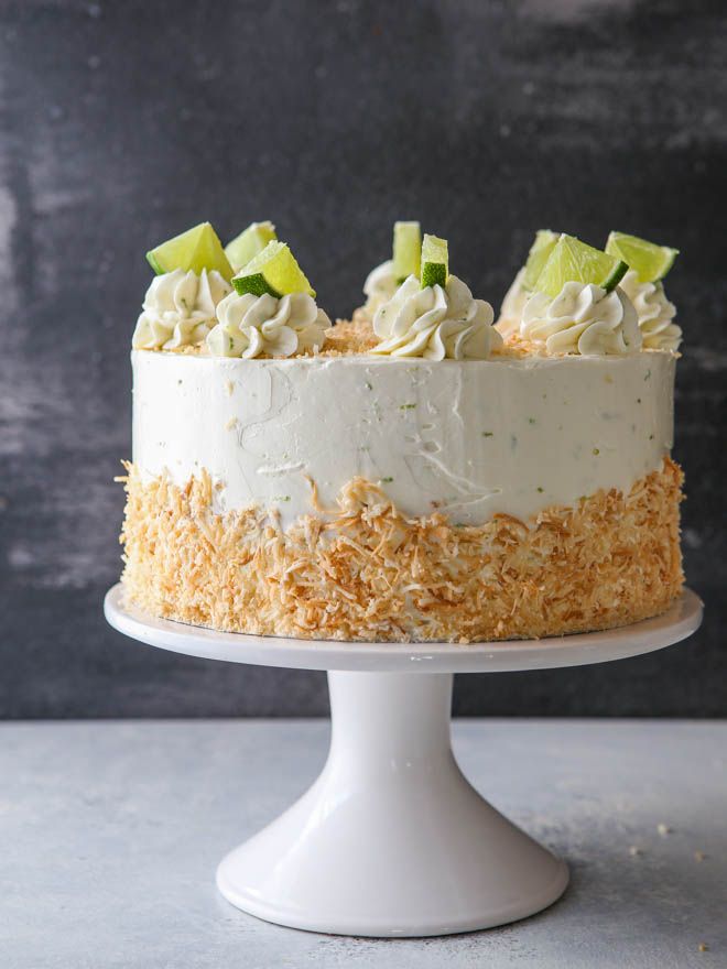 a cake with white frosting and limes on top is sitting on a pedestal