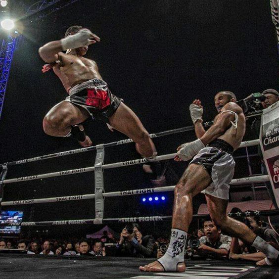 two men in the middle of a boxing ring, one kicking another with his leg