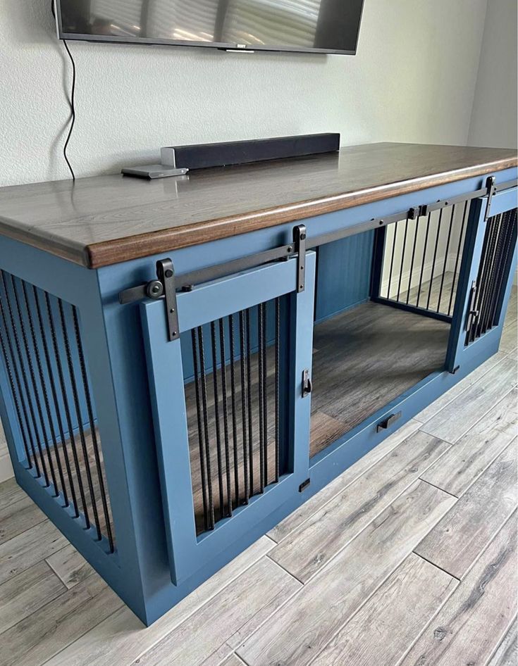 a dog kennel in front of a flat screen tv on top of a wooden table