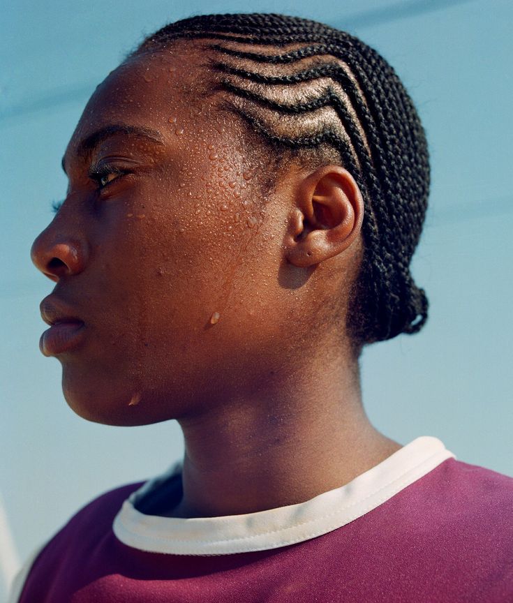 a woman with braids on her hair looks off to the side while wearing a purple shirt