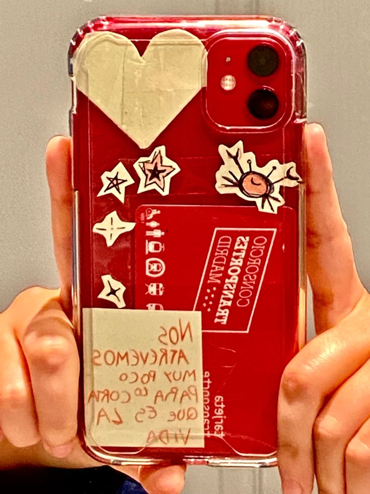 a person holding up a red phone case with stickers on it's back