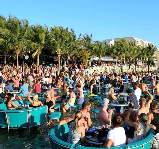 a large group of people are sitting in small boats on the water, with palm trees behind them