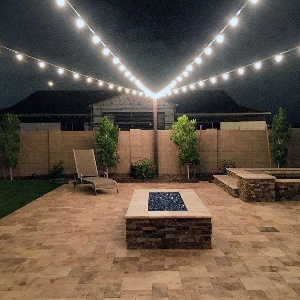 an outdoor patio with lights strung over it and chairs around the fire pit in the middle