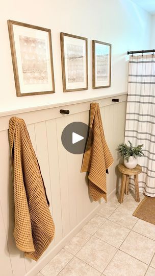 a bathroom with three towels hanging on the wall and two pictures above it, along with a stool