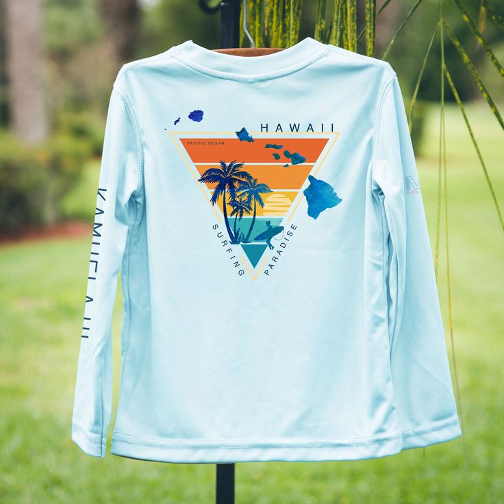 a shirt hanging on a stand in the grass with palm trees and blue sky behind it