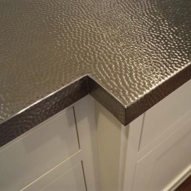 a kitchen counter top that is made out of metal and white cabinets with wood flooring