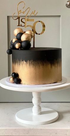 a black and gold birthday cake on a white pedestal with the number fifty one in gold