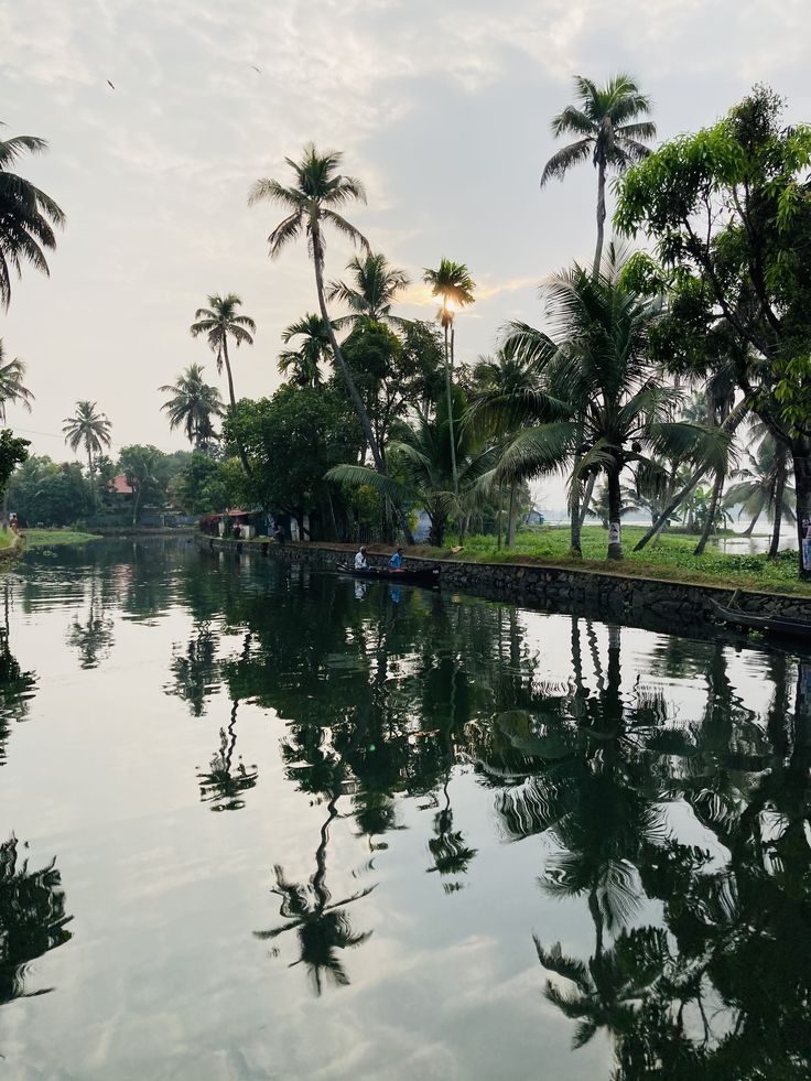 the water is reflecting palm trees and people in boats on the other side of the river