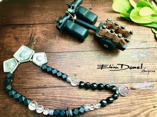 the black and white beaded necklace is laying on top of a wooden table next to flowers